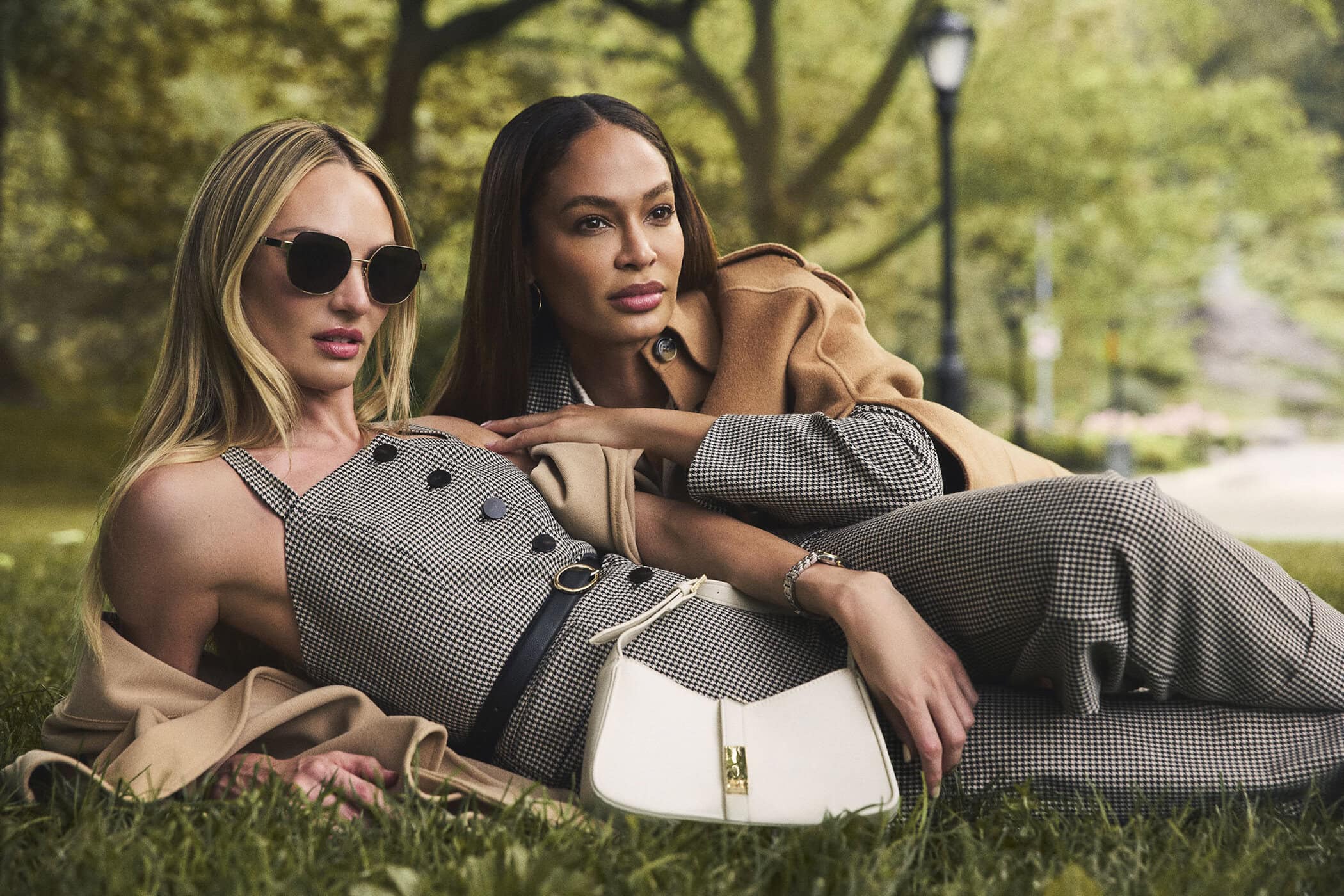 Candice Swanepoel and Joan Smalls lying on grass wearing houndstooth outfits and a camel coat for Anne Klein Fall 2025 campaign.
