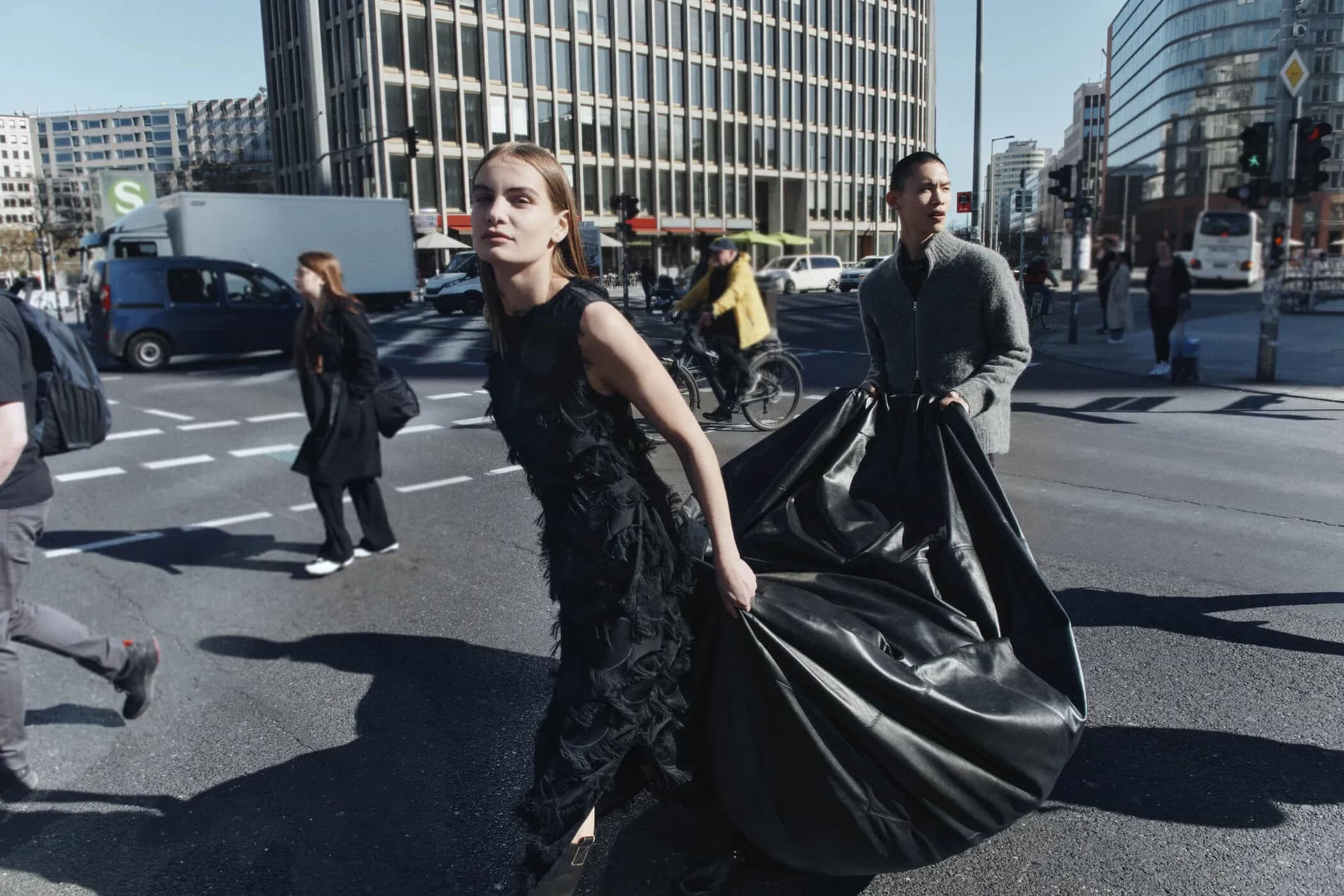 Models walking on a city street in Berlin for Samsoe Samsoe, holding a large black sculptural bag.