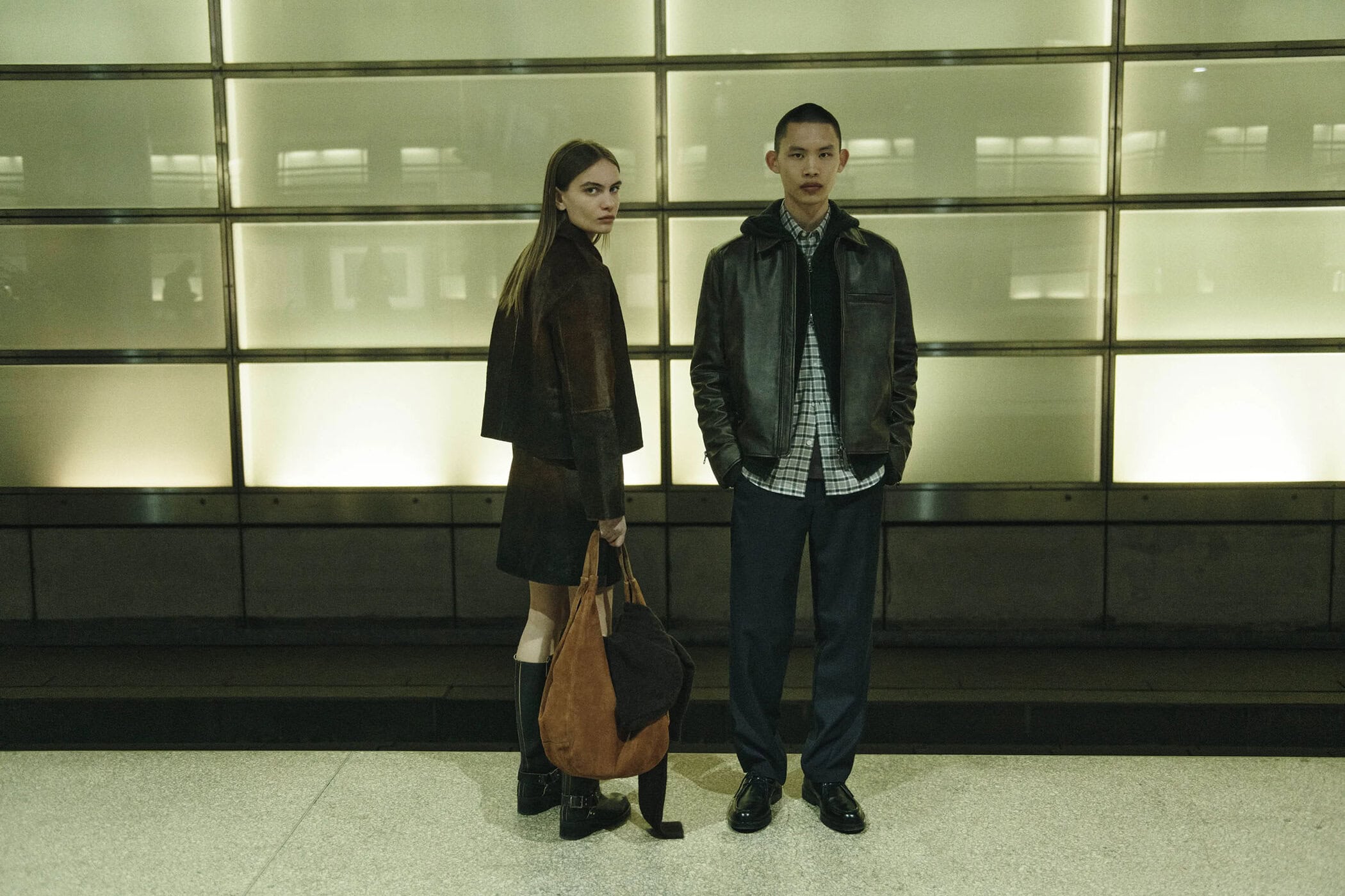 Two models standing against an illuminated gridded wall in an urban setting for Samsoe Samsoe fall 2025 ad campaign.