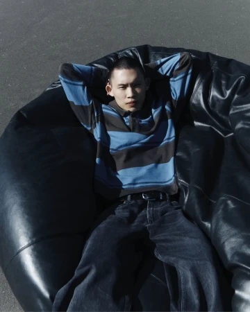 Man wearing a blue striped polo shirt lounging on a black leather bean bag chair outdoors.