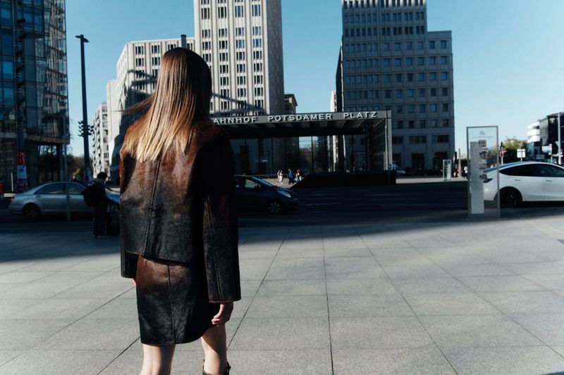 Model walking away from camera wearing a brown leather jacket and skirt at Berlin Potsdamer Platz.