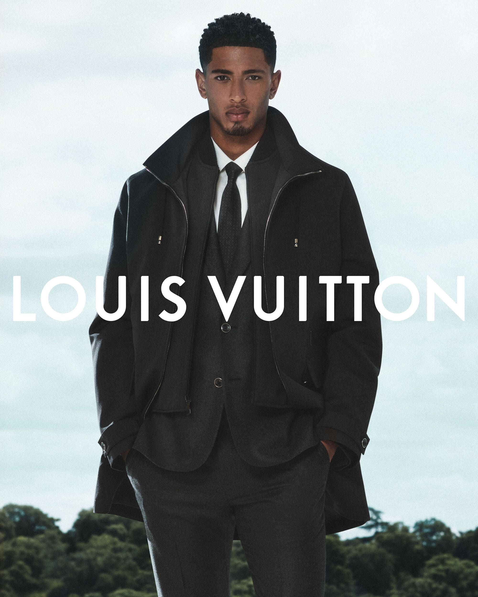 Jude Bellingham wearing a black suit and jacket for Louis Vuitton against an open sky background
