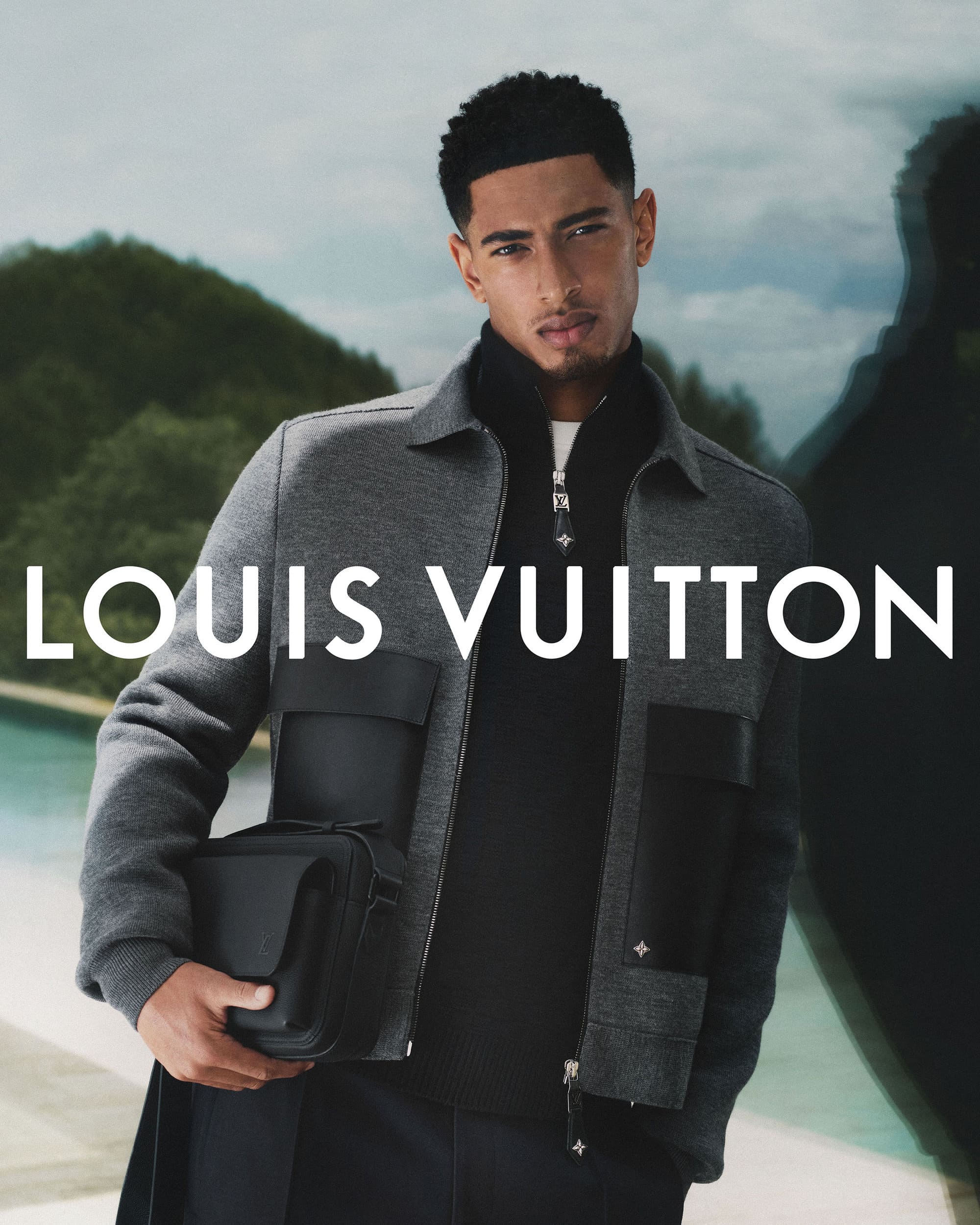 Jude Bellingham wearing a grey jacket over a black sweater, holding a black handbag for a Louis Vuitton campaign.