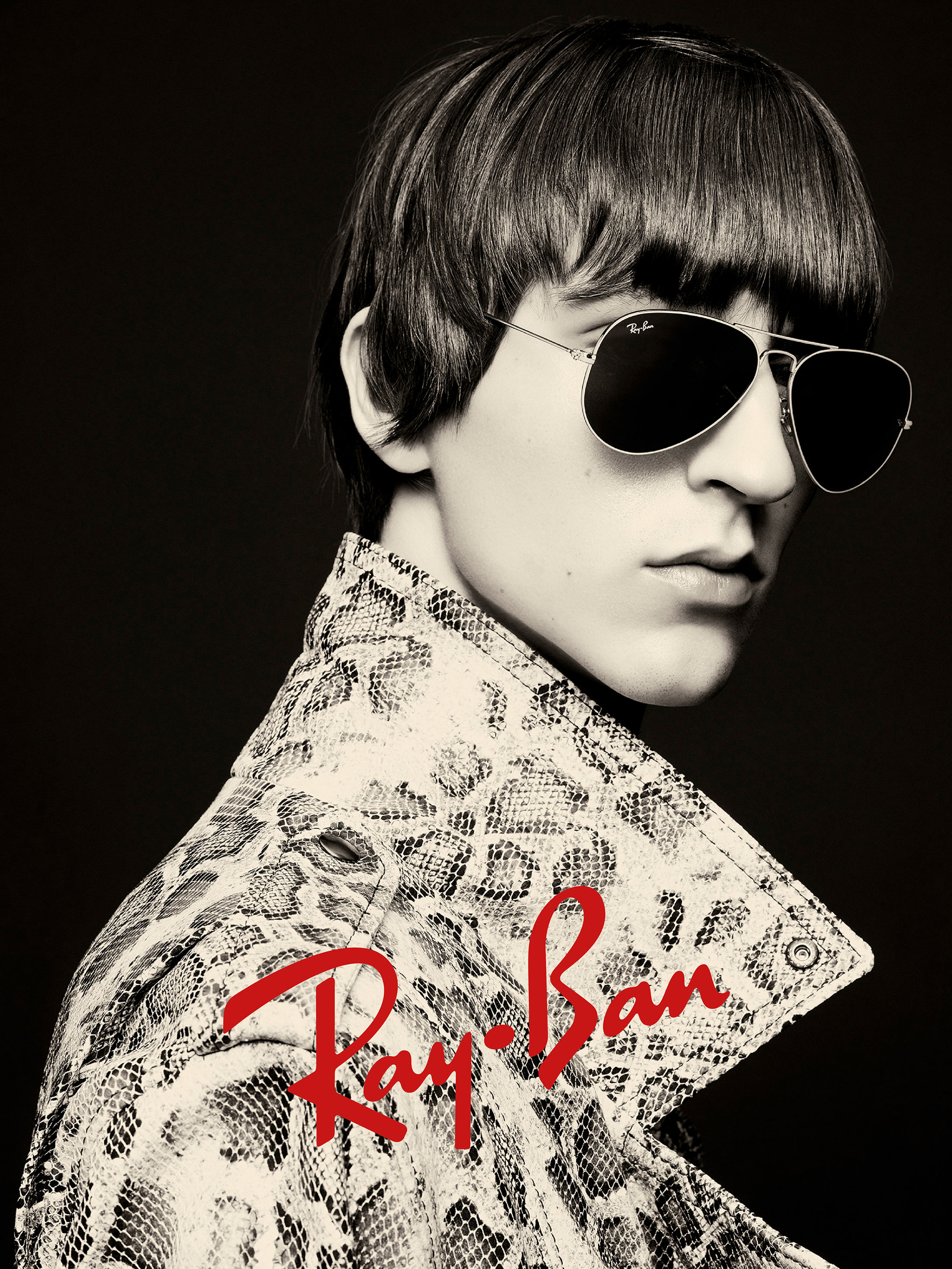 Model wearing dark aviator sunglasses and a snakeskin patterned jacket against a dark background with Ray-Ban logo