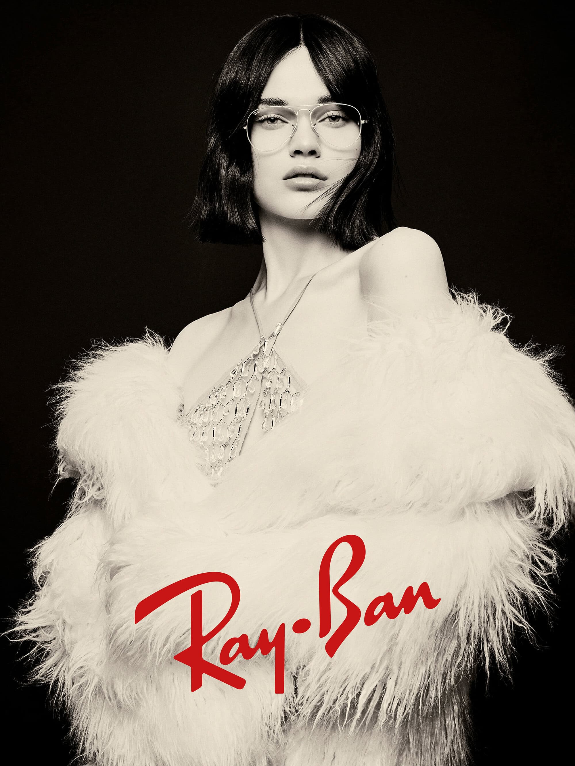 Model wearing eyeglasses and a fluffy white coat with the Ray-Ban logo overlay against a dark background