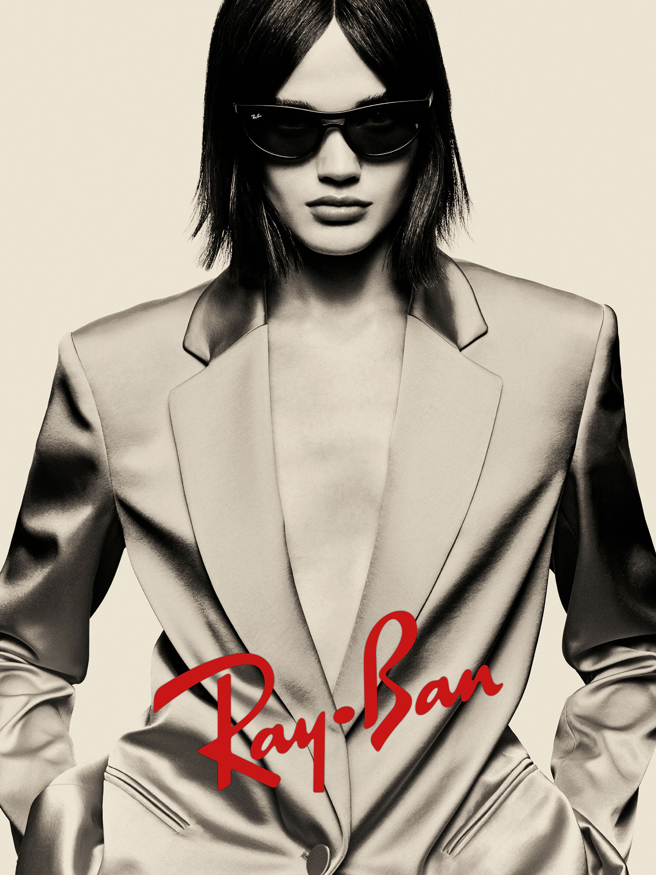 Model wearing dark sunglasses and a tailored blazer against a pale background for Ray-Ban campaign