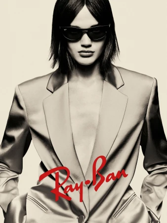 Model wearing dark sunglasses and a tailored blazer against a pale background for Ray-Ban campaign