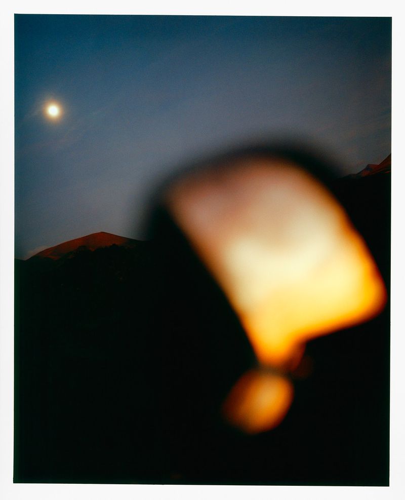 Night scene featuring a blurry foreground shape with a mountain range and a full moon in the sky, creating a moody atmosphere.