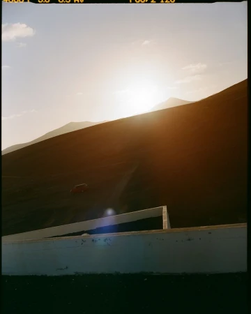 Tranquil landscape featuring a hillside with sun and sky, complemented by a concrete structure in the foreground, creating a serene scene.