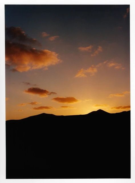 Dramatic sunset landscape featuring silhouetted mountain range against a sky with colorful orange and peach-colored clouds.