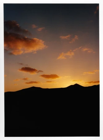 Dramatic sunset landscape featuring silhouetted mountain range against a sky with colorful orange and peach-colored clouds.