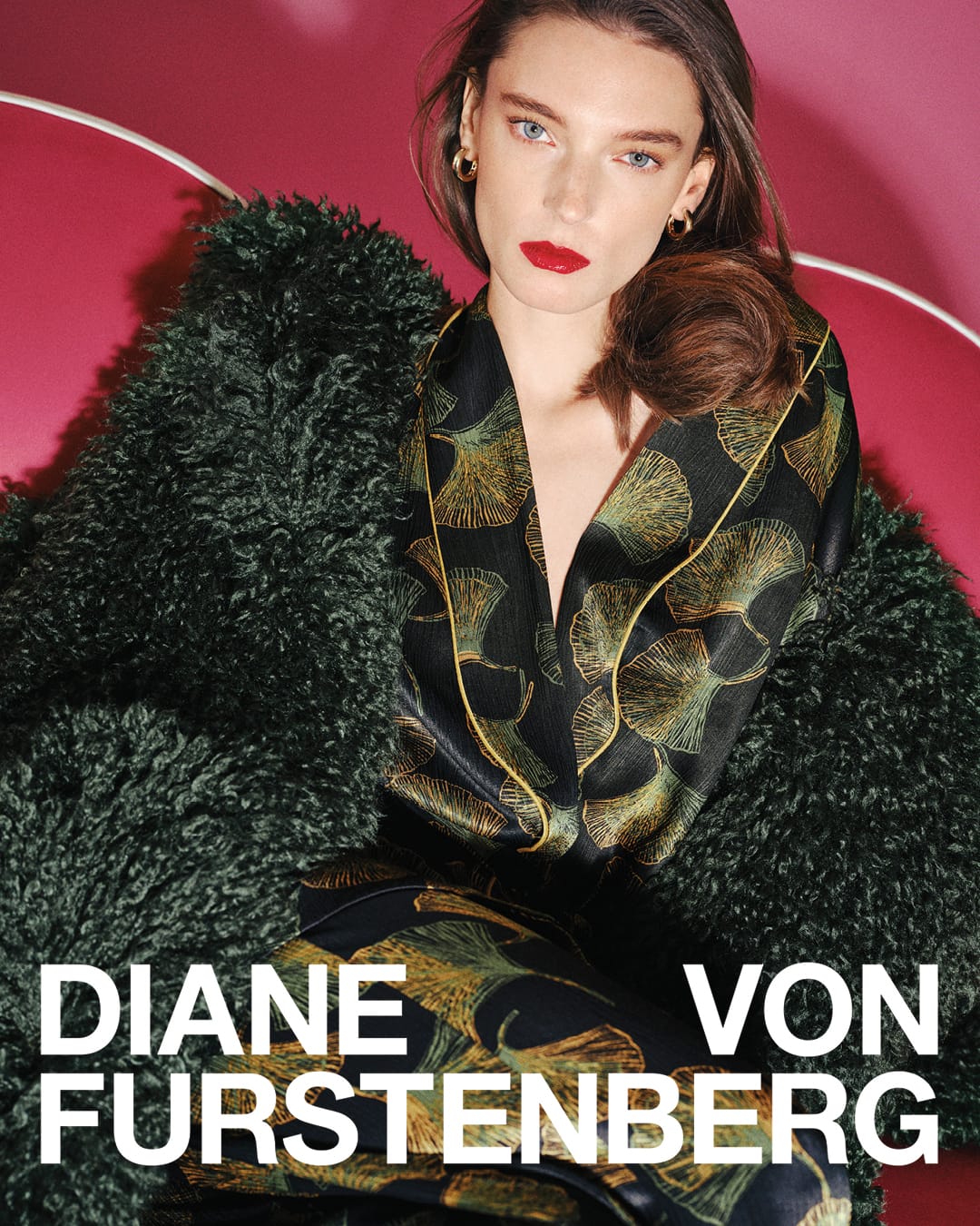 Model in printed silk top wearing a green fuzzy coat against a deep pink setting for Diane von Furstenberg Fall 2025 campaign.
