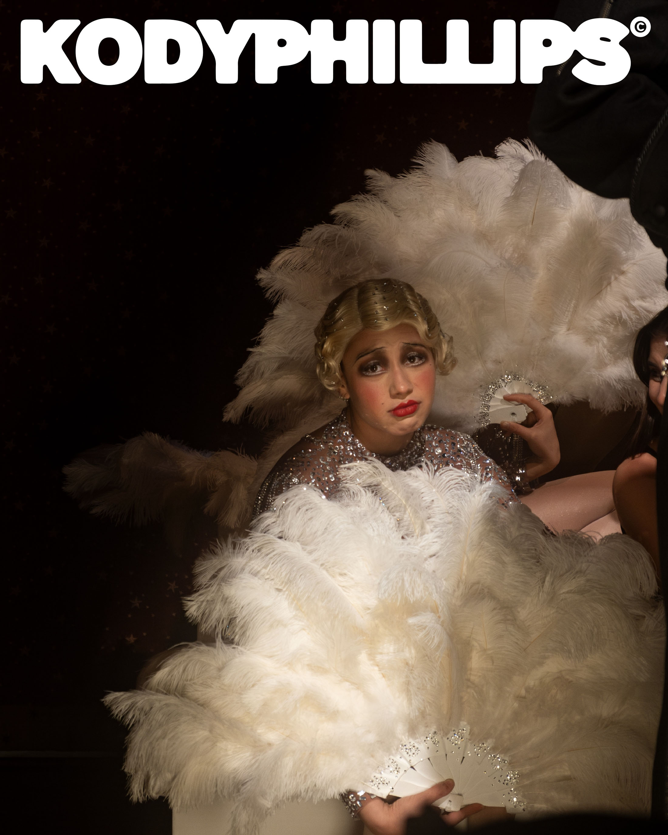 Model in vintage feathered headdress and sequined top holding white feather fans for Kody Phillips ad campaign.