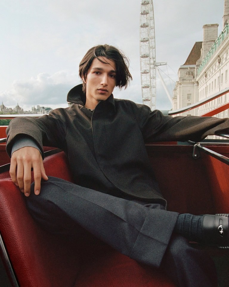 A man seated in a red vehicle cabin with the London Eye visible in the background for a Burberry campaign.