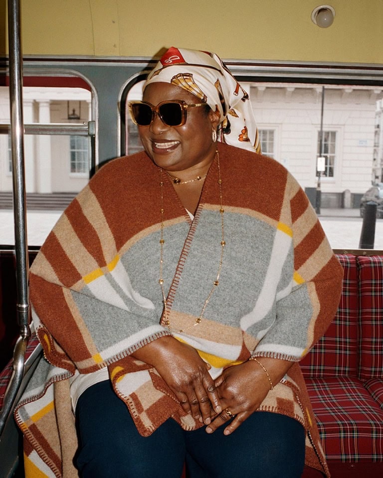 Model wearing a plaid poncho and patterned headscarf on a bus for Burberry Back to the City campaign