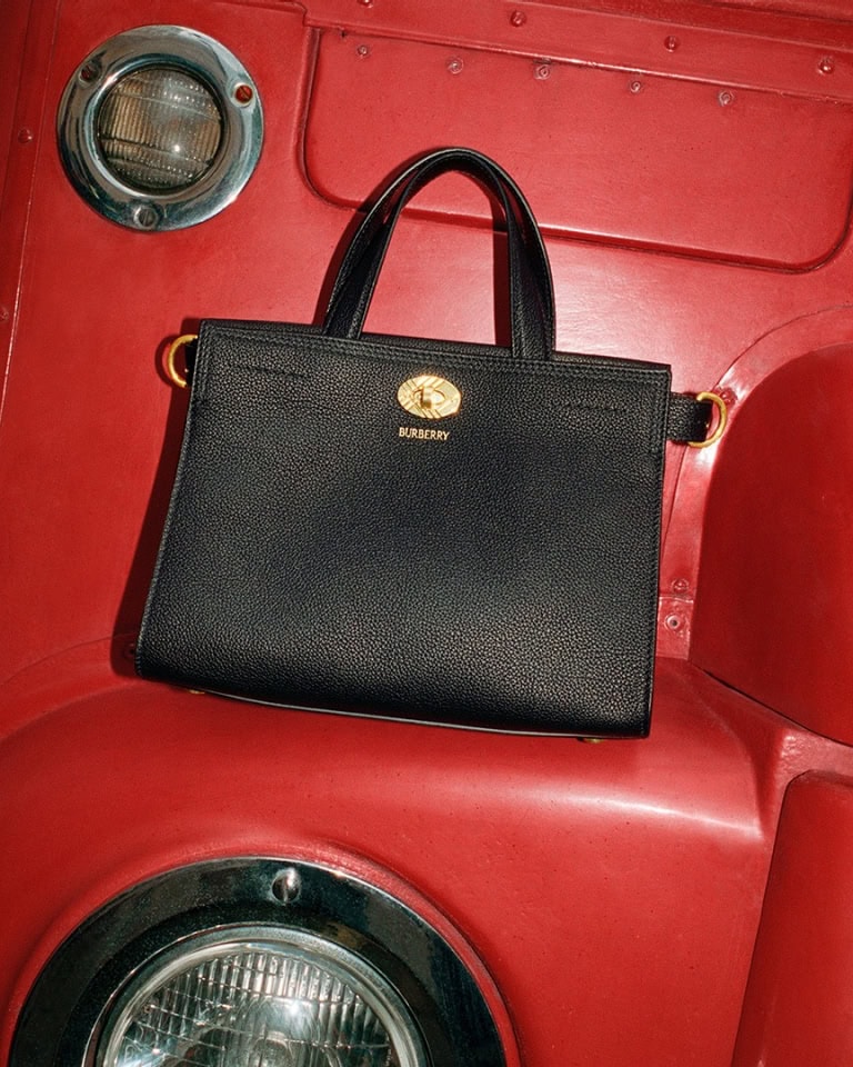 Black leather handbag with gold hardware resting against a bright red textured vehicle surface