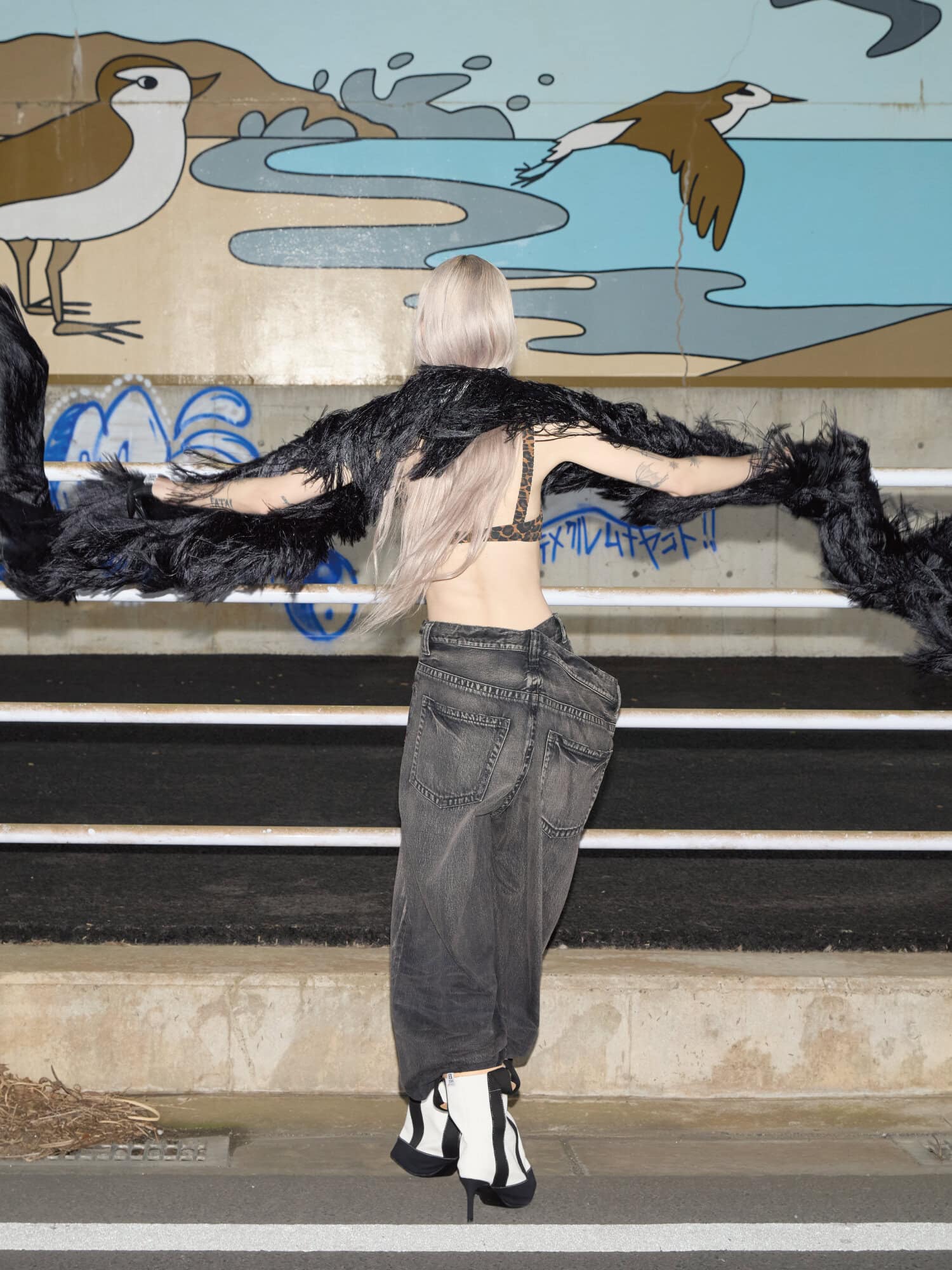 Model with long blonde hair seen from behind wearing black textured scarf and oversized dark denim jeans.