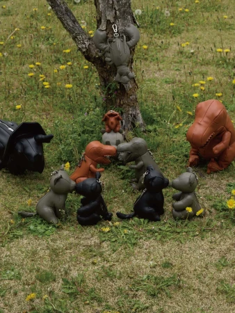Collection of leather dinosaur and animal shaped bag charms arranged on a grassy patch around a tree trunk for Maison Mihara Yasuhiro.