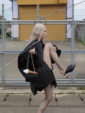 Model with long blonde hair wearing a black bomber jacket and fishnet tights holding a black handbag with an ice cream prop