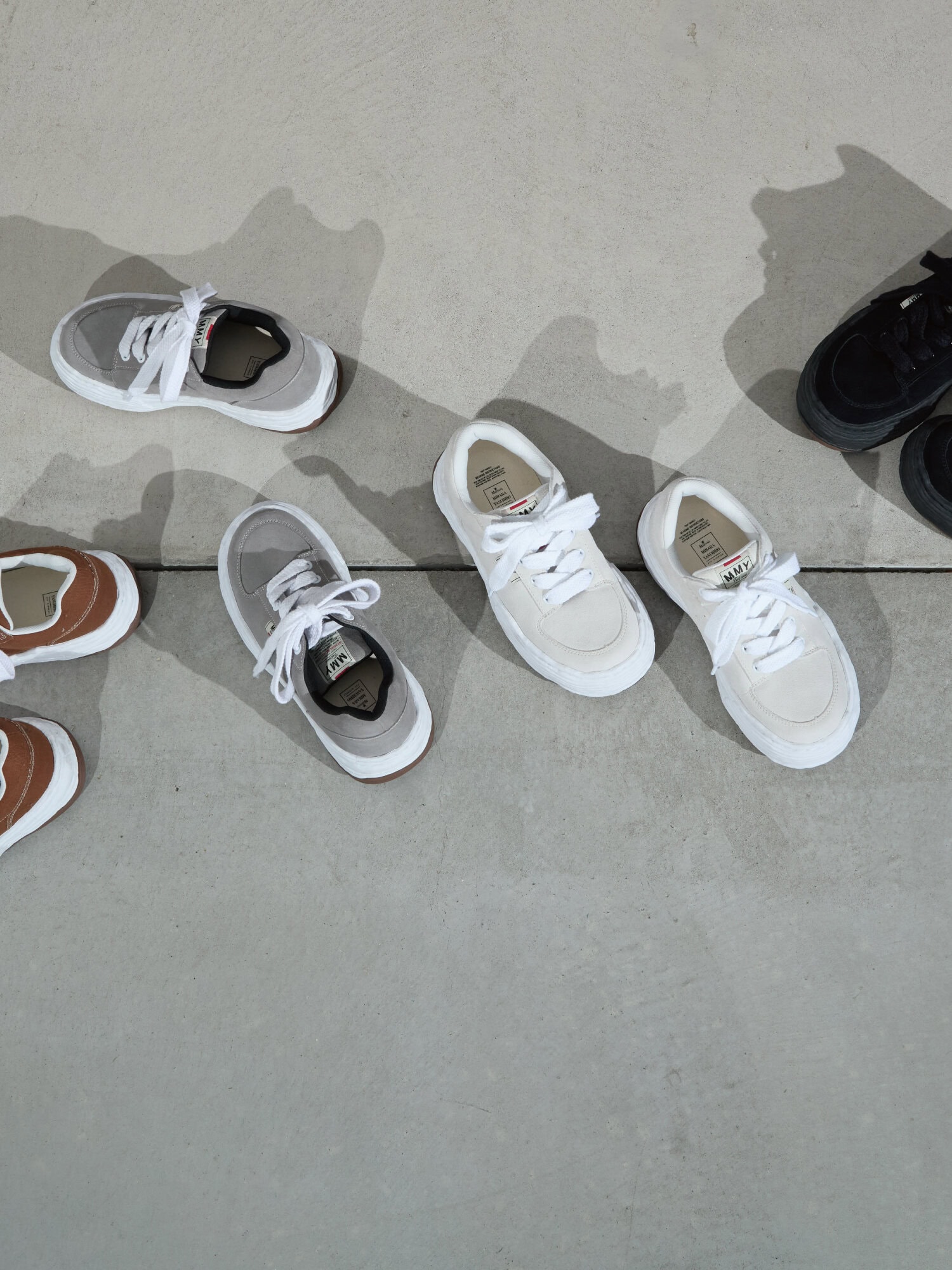 Top-down view of several pairs of low-top sneakers in assorted colors arranged on a concrete ground surface.