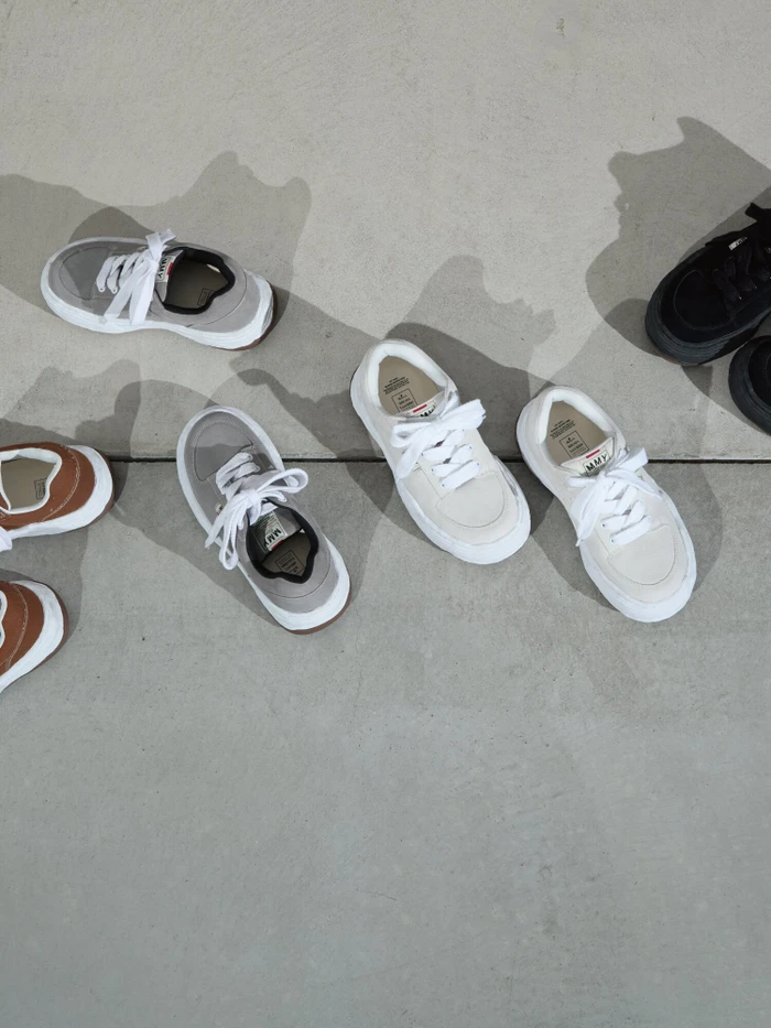 Top-down view of several pairs of low-top sneakers in assorted colors arranged on a concrete ground surface.