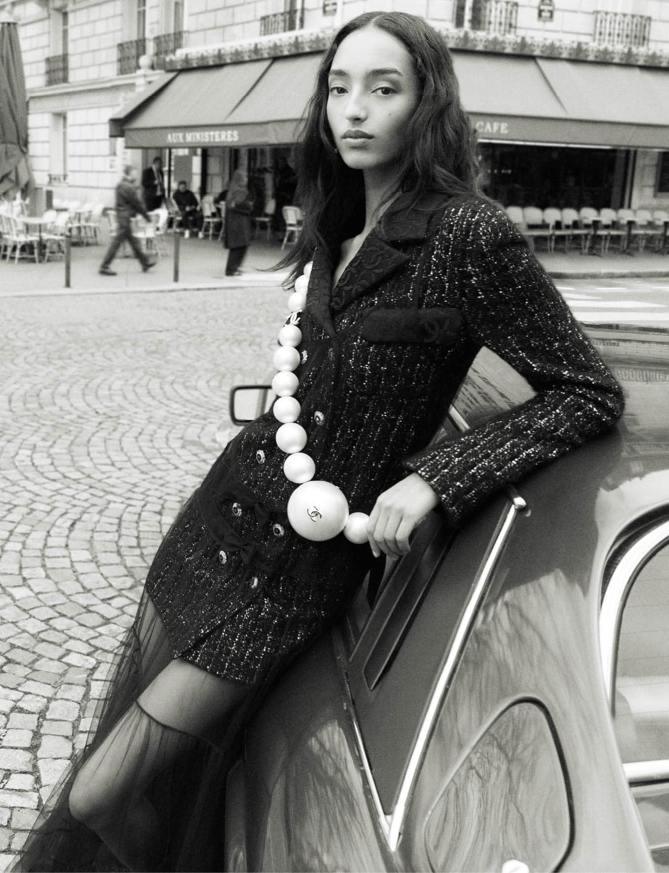 Mona Tougaard leaning against a car on a Paris street wearing a tweed jacket with a large pearl necklace for Chanel