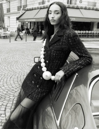 Mona Tougaard leaning against a car on a Paris street wearing a tweed jacket with a large pearl necklace for Chanel