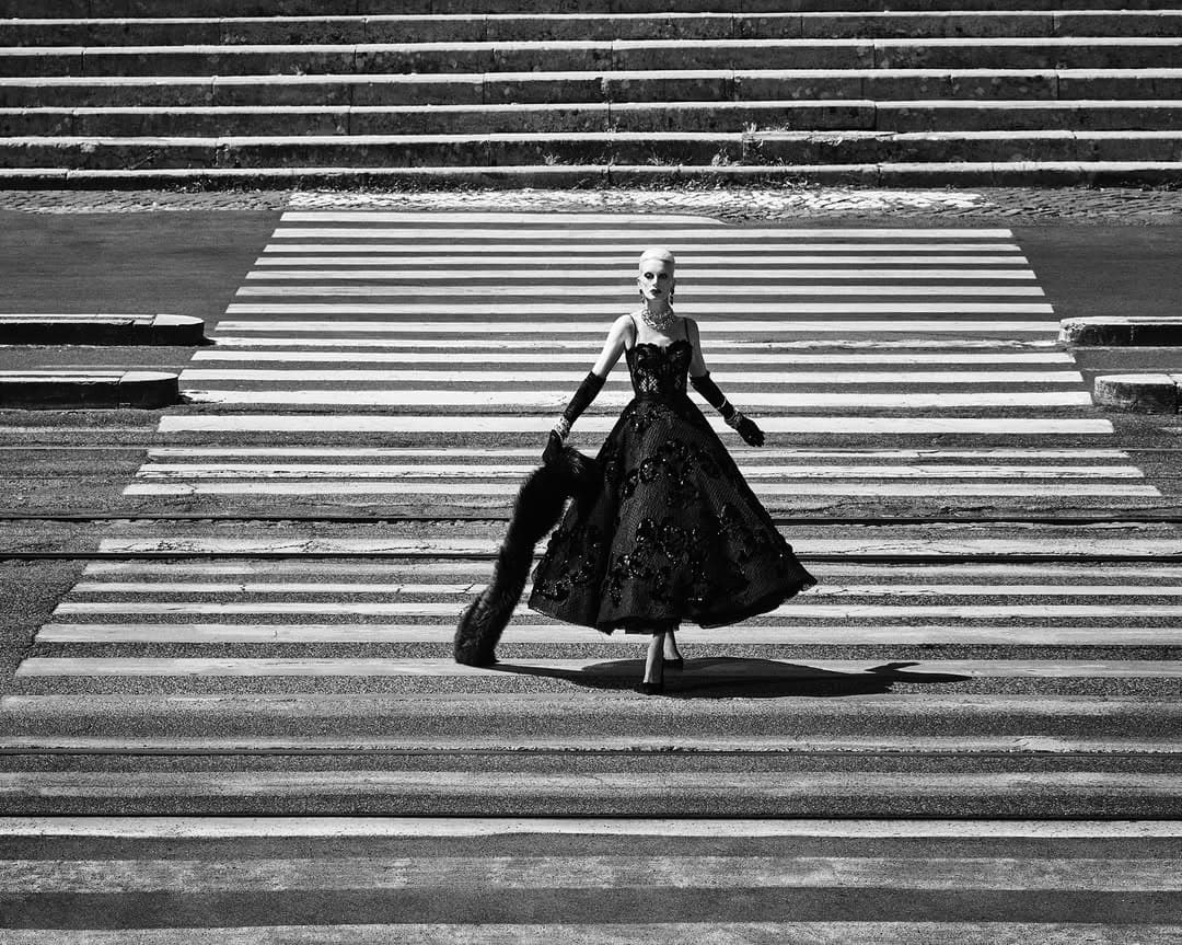 Model Kristen McMenamy in a black gown on a crosswalk for Dolce and Gabbana Alta Moda