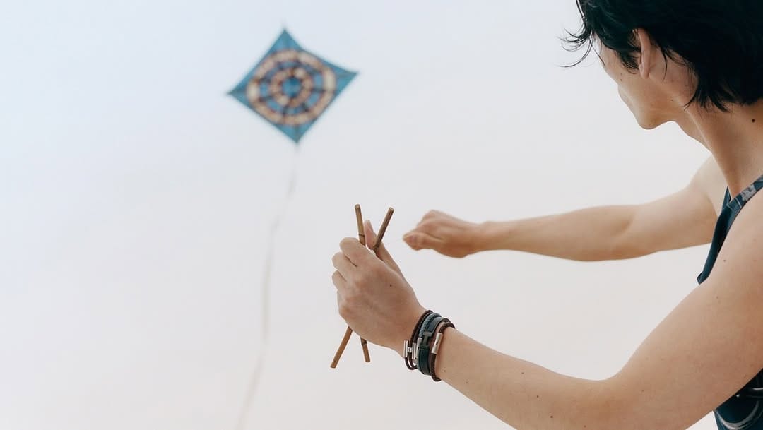Man holding wooden sticks flying a blue patterned kite against an open sky for Hermes summer 2025 ad campaign.