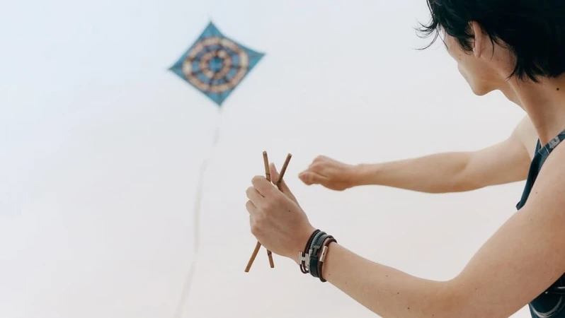 Man holding wooden sticks flying a blue patterned kite against an open sky for Hermes summer 2025 ad campaign.