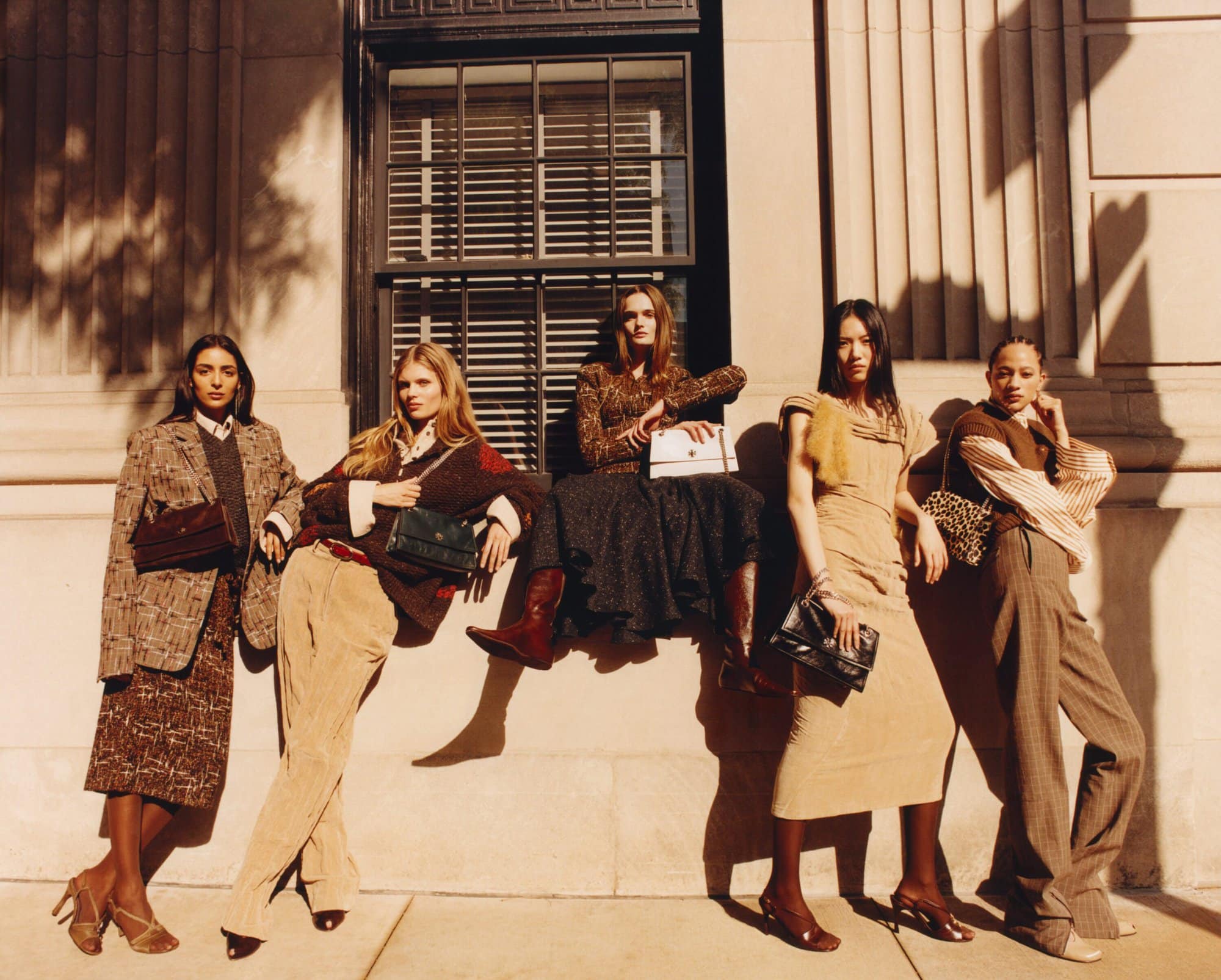 Group of five female models posing against a stone building exterior with tall windows for Tory Burch Fall 2025 campaign