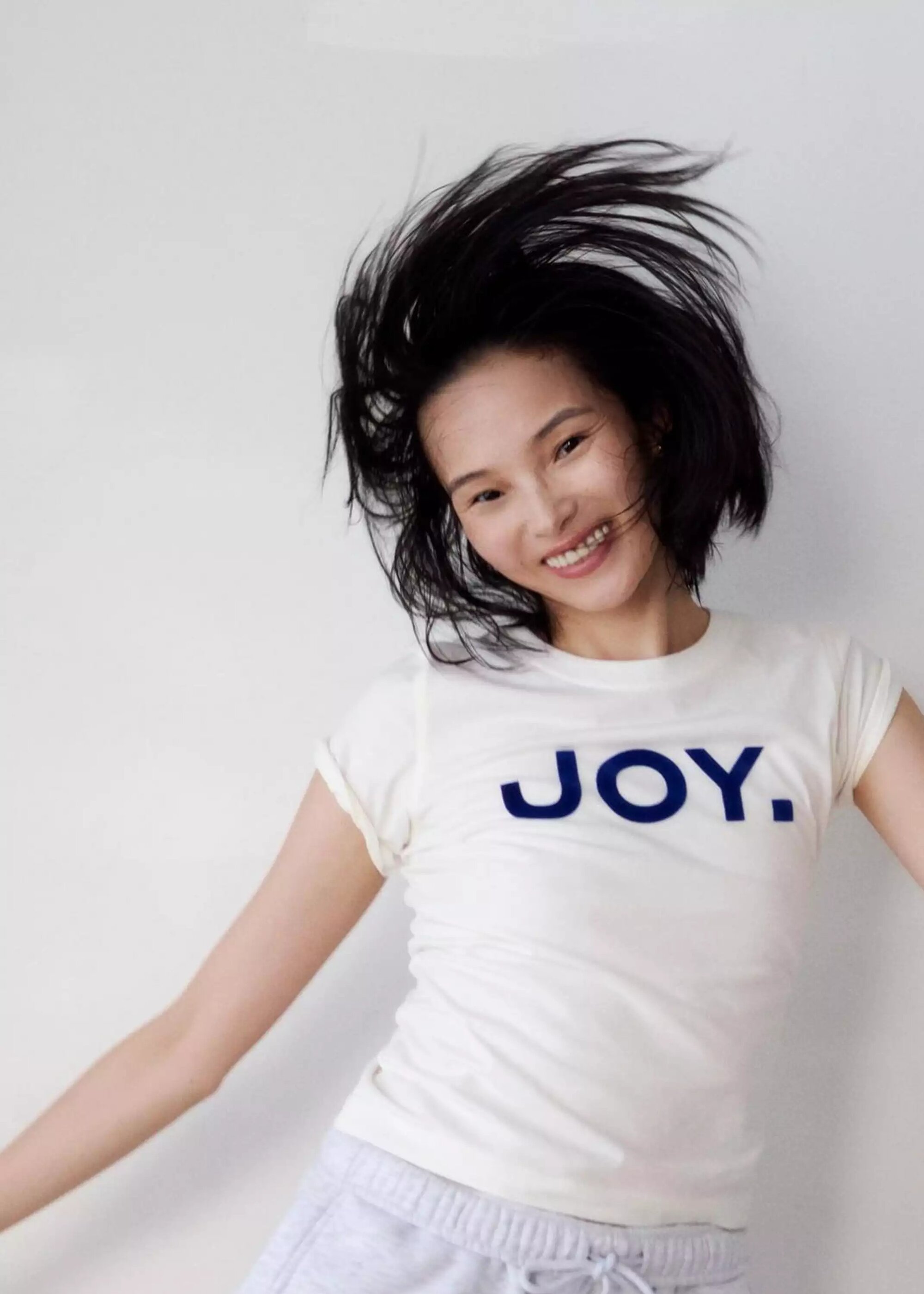 Model with dark hair swishing around her face wearing a white t-shirt with blue text against a seamless white background