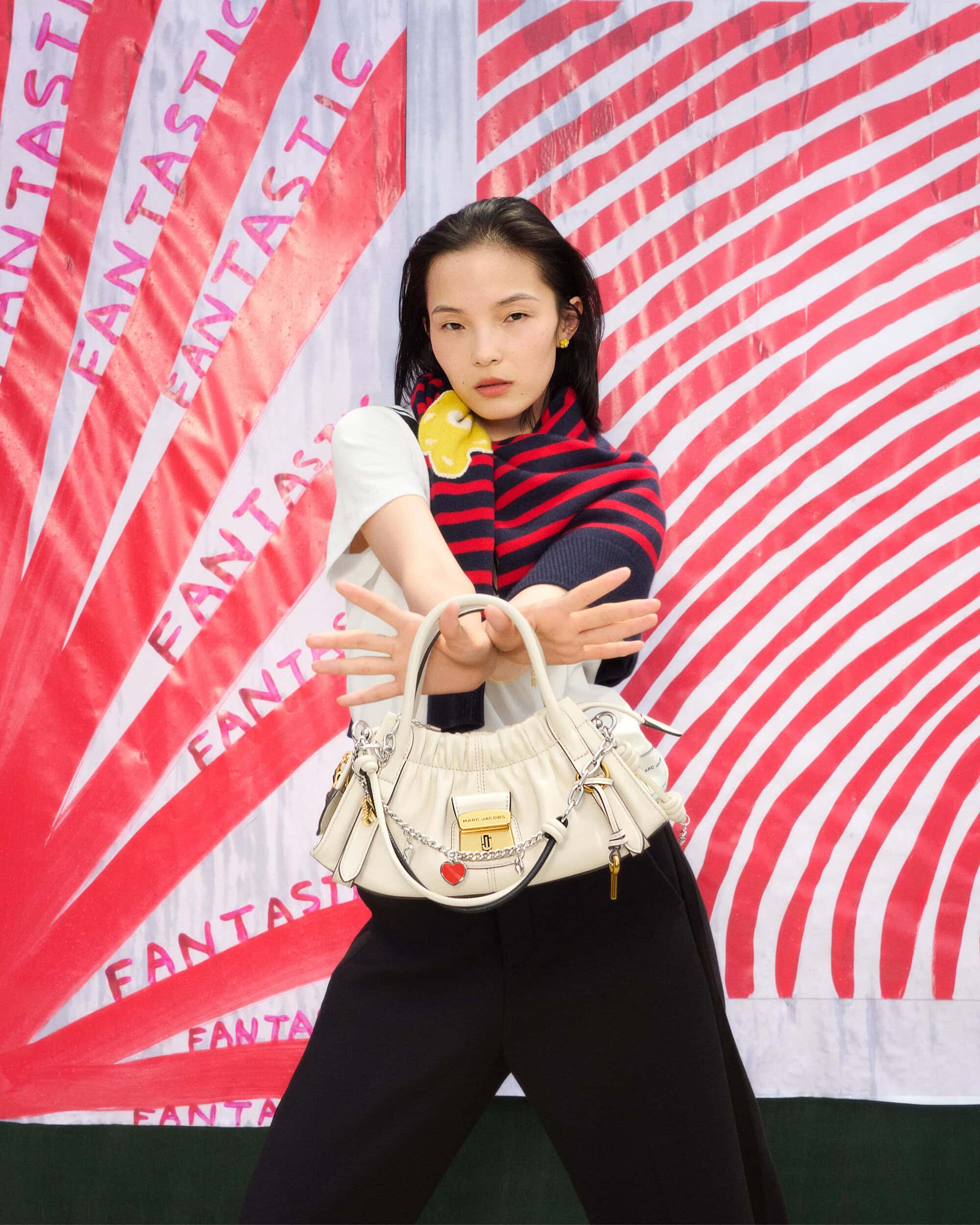 Model holding a white leather handbag against a red and white striped background with repeated text for Marc Jacobs Fall 2025 campaign