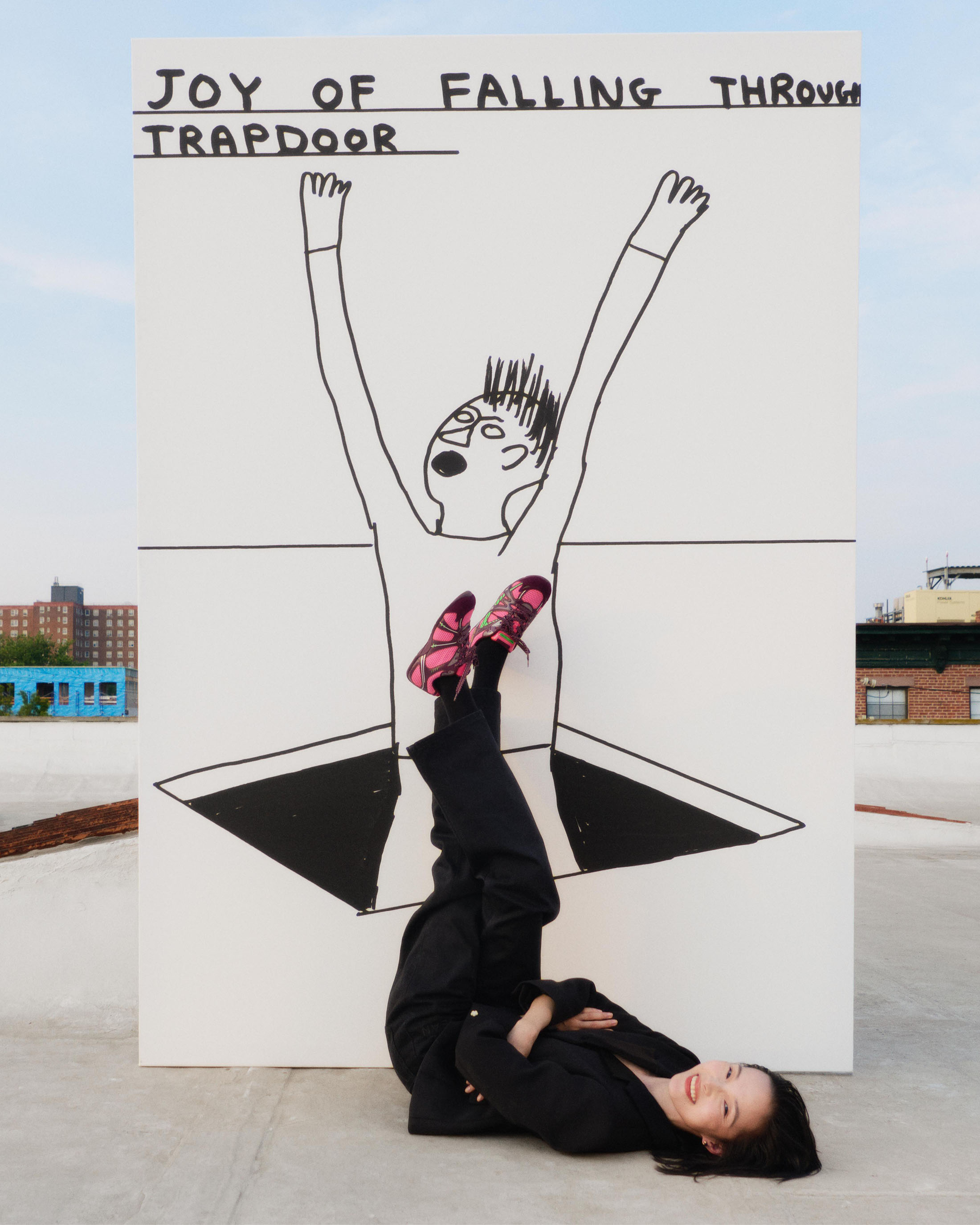 A person lying on a rooftop beneath a large hand-drawn art panel featuring a figure falling through a trapdoor.