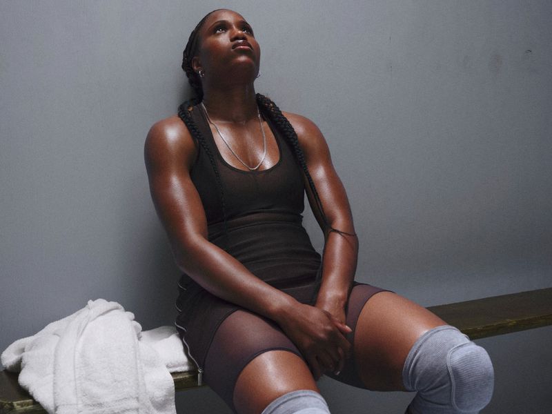 Athletic Black woman sitting on a bench in sportswear with knee pads in locker room looking up in an eye-level medium shot, head and shoulders.