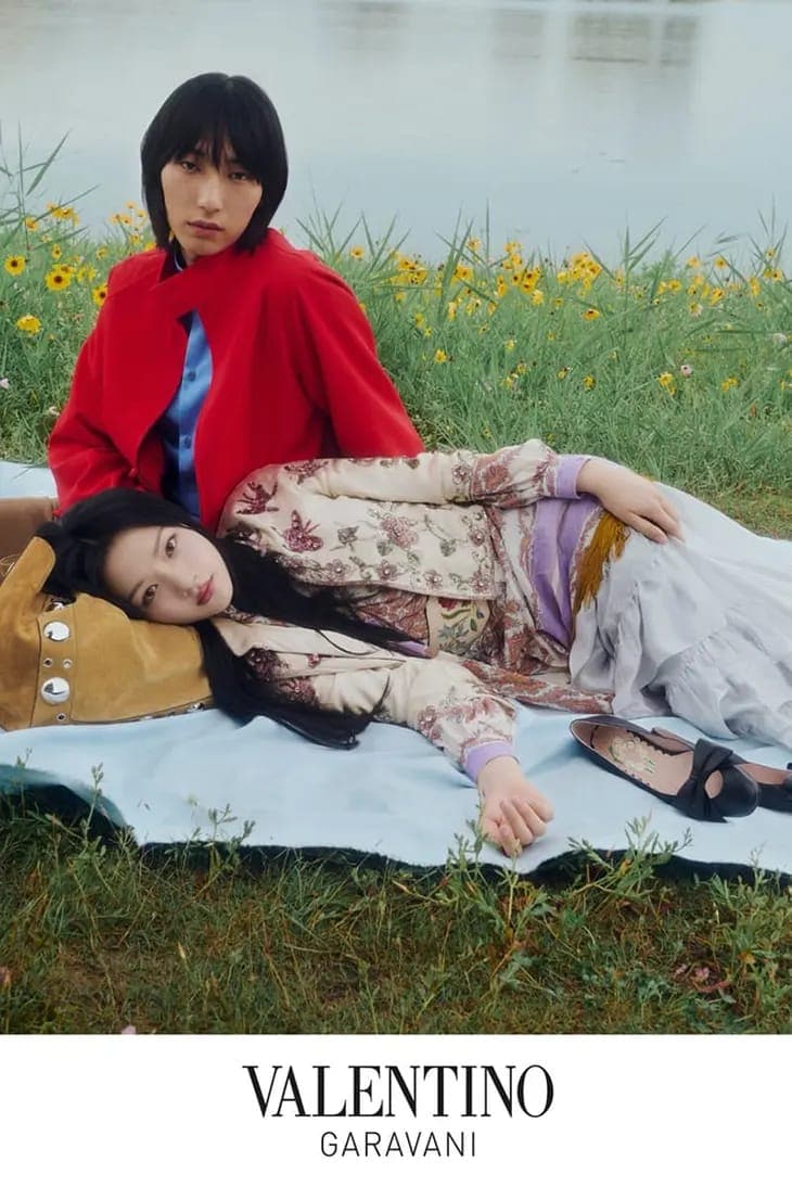 Two models resting on a light blue blanket outdoors near a body of water, photographed by Julie Greve for Valentino.