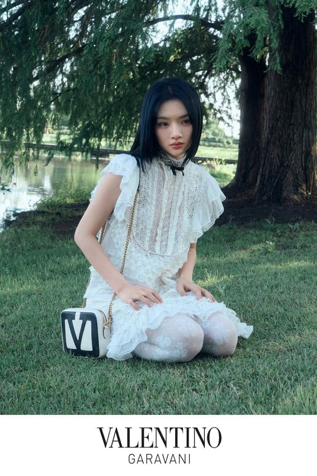 Woman in white lace dress kneeling on grass next to a water body with a structured handbag for Valentino Chinese Valentine's Day campaign
