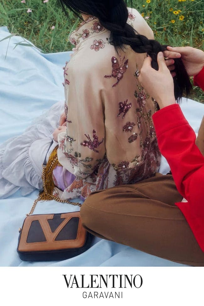 Two people outdoors on a blue blanket with an embroidered top and a Valentino Garavani handbag.