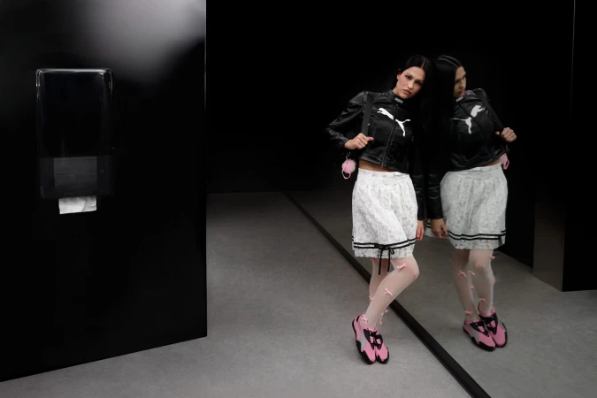 Model Amelia Gray in a black Puma leather jacket and white skirt standing near a dark reflective surface for the Mostro Ad Campaign.