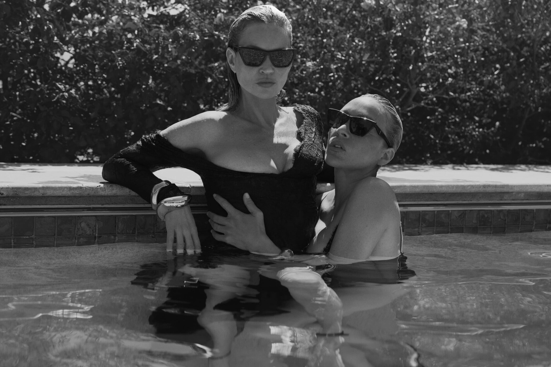 Kate Moss and Chloë Sevigny posing in a swimming pool wearing black sunglasses and black attire for Saint Laurent.