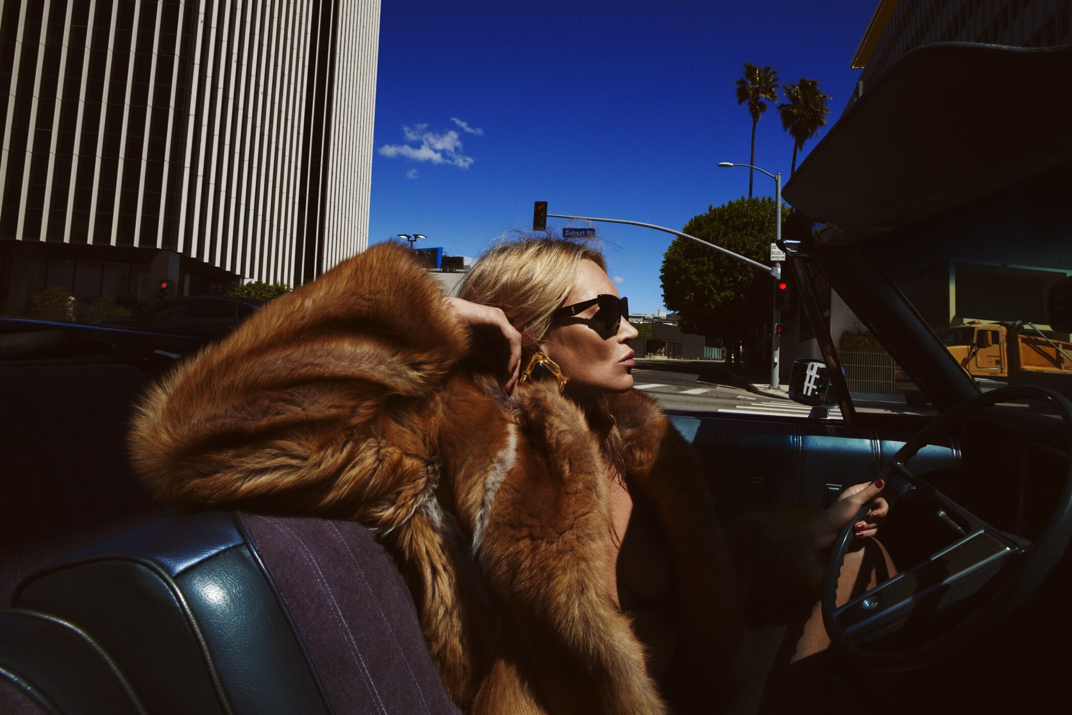 Kate Moss wearing a fur coat and sunglasses while driving a vintage convertible in Los Angeles