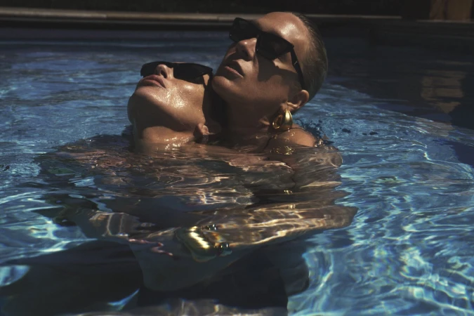 Kate Moss and Chloë Sevigny wearing sunglasses in a swimming pool for Saint Laurent Pre-Fall 2025 ad campaign by Mert Alas