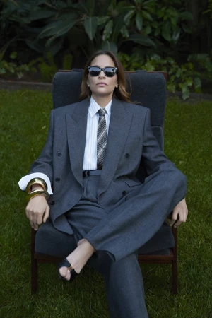Model wearing a grey suit and sunglasses seated in an outdoor armchair for Saint Laurent Pre-Fall 2025 campaign