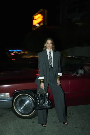 Chloë Sevigny in a grey suit leaning against a vintage red car at night for Saint Laurent