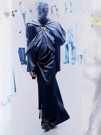Model wearing a dark satin gown and patterned head covering standing against a blurred background