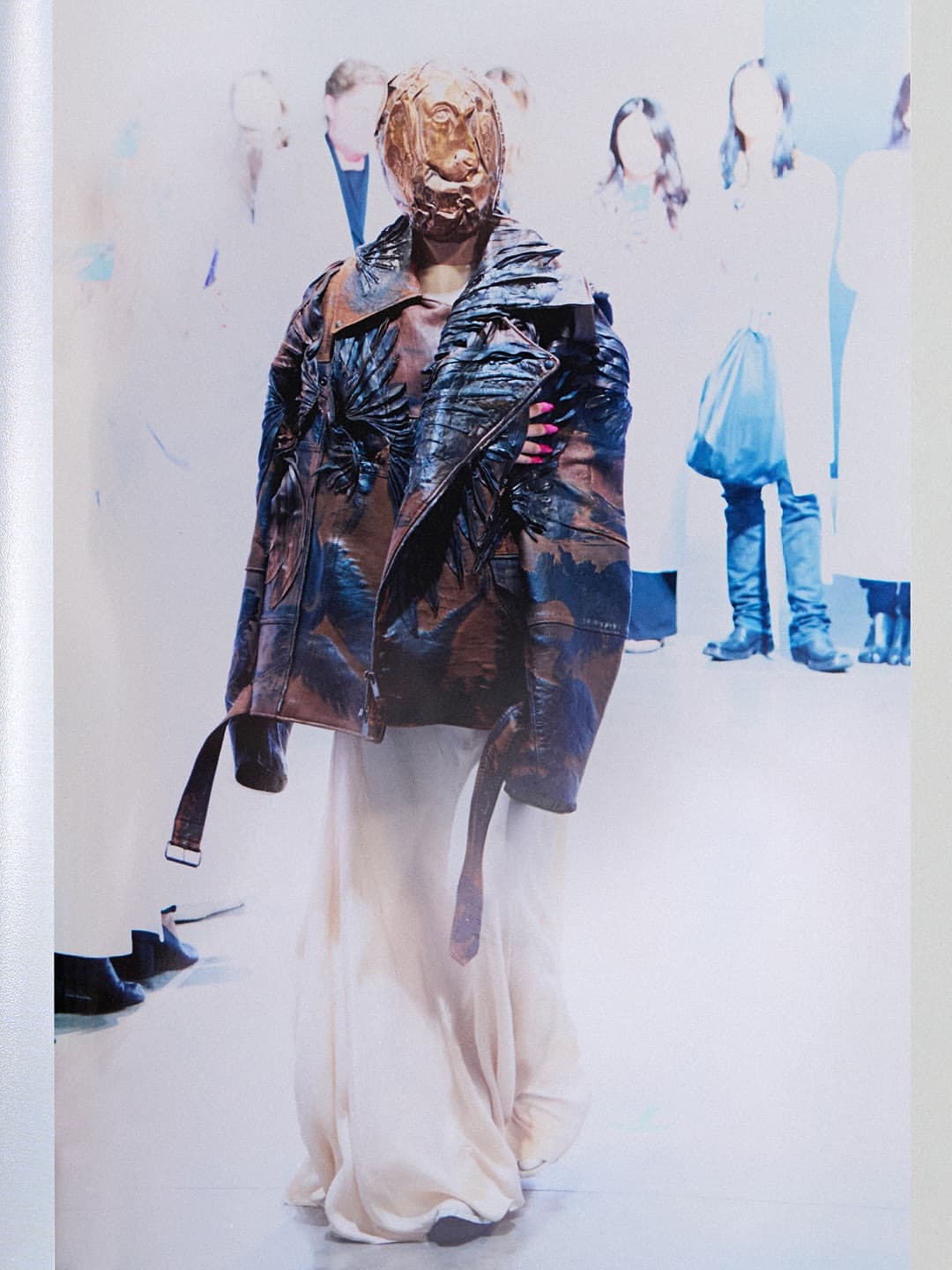 Model wearing a sculpted mask and patterned leather jacket with a long white skirt for Maison Margiela Artisanal campaign