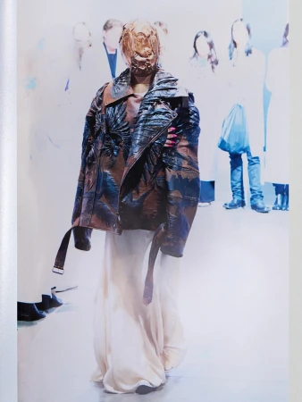 Model wearing a sculpted mask and patterned leather jacket with a long white skirt for Maison Margiela Artisanal campaign