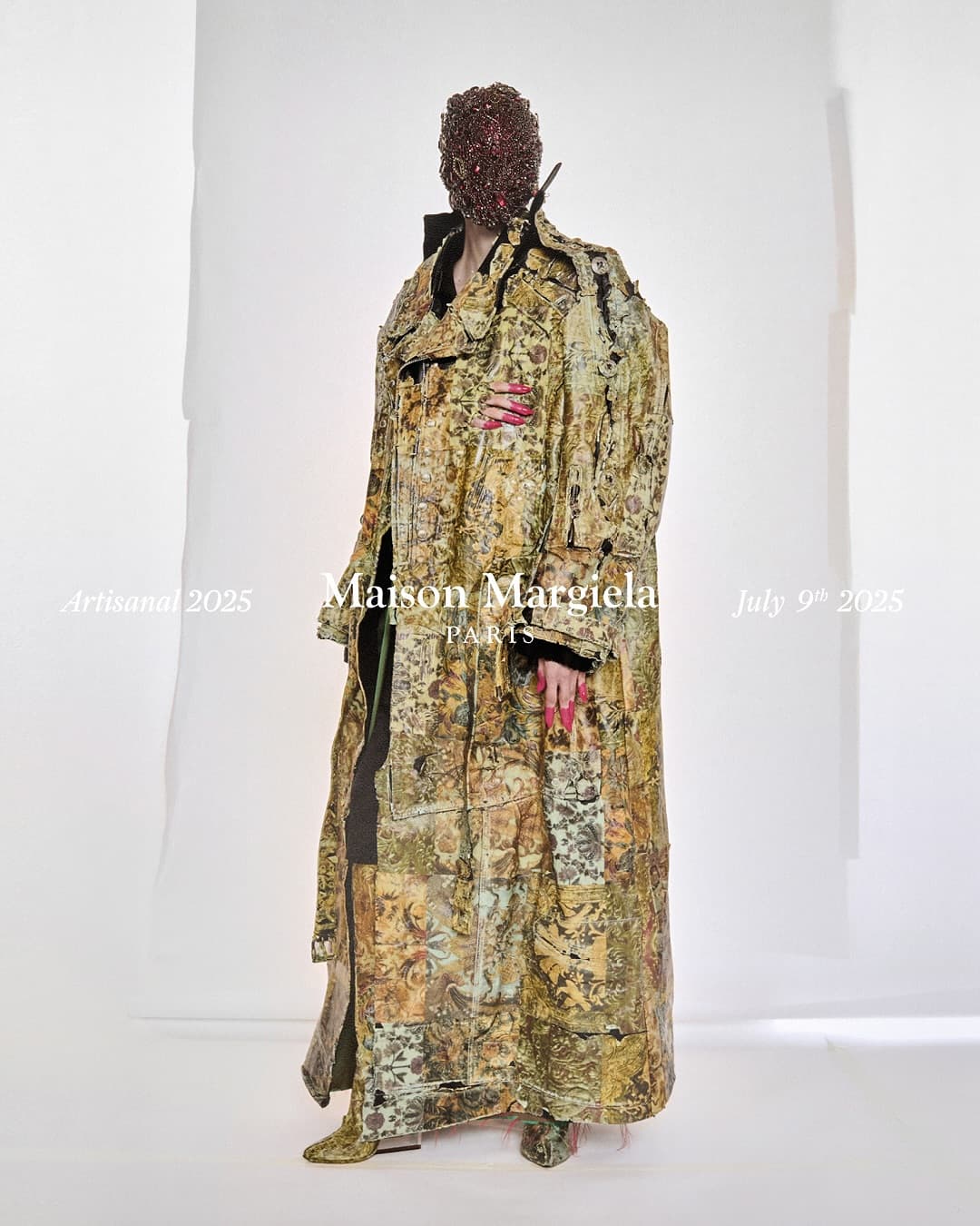 Model wearing an ornate patterned coat and beaded headpiece against a white seamless background
