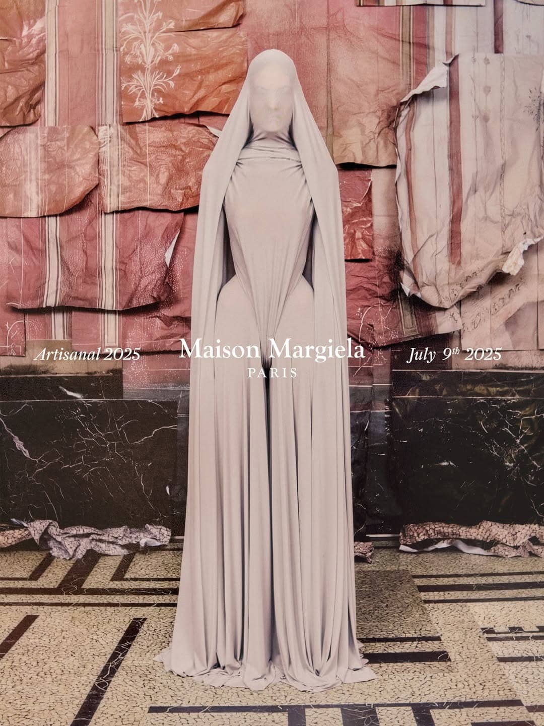 Model wearing a veiled hooded gown with sculptural lines standing against a textured paper collage wall.