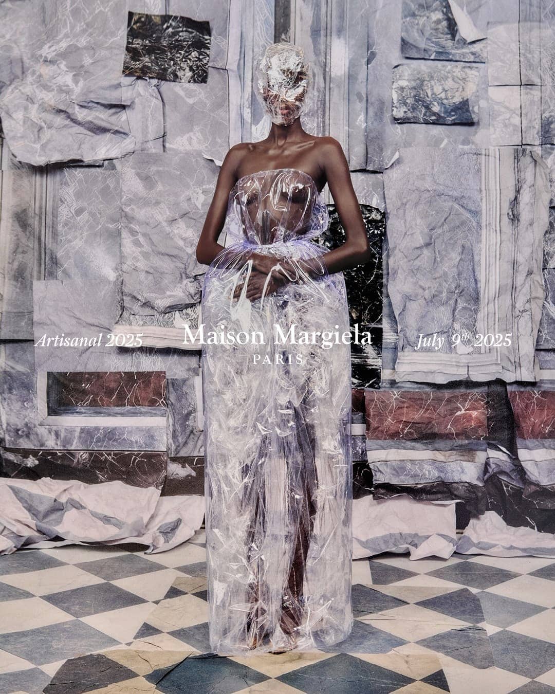 Model standing centrally wearing a translucent plastic structured gown against a collaged grey wall and checkerboard floor